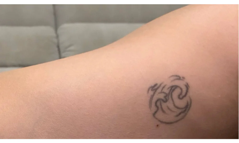 Minimalist fine line tattoo of a wave on arm, representing a simple and elegant design with personal meaning.
