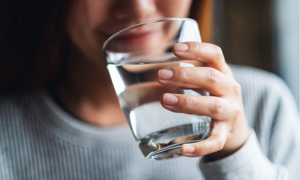 Close-up image of a woman drinking water from a glass, underlining the necessity of staying hydrated before getting a tattoo.