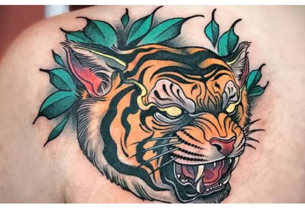 Neo Traditional tattoo of a tiger head on shoulder, showcasing vibrant colors, detailed shading, and decorative leaves.