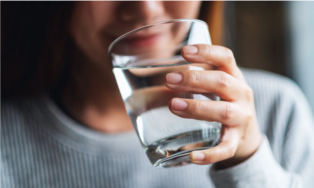 A close-up of a person holding a glass of water, emphasizing the importance of staying hydrated for healthy skin and optimal tattoo healing.