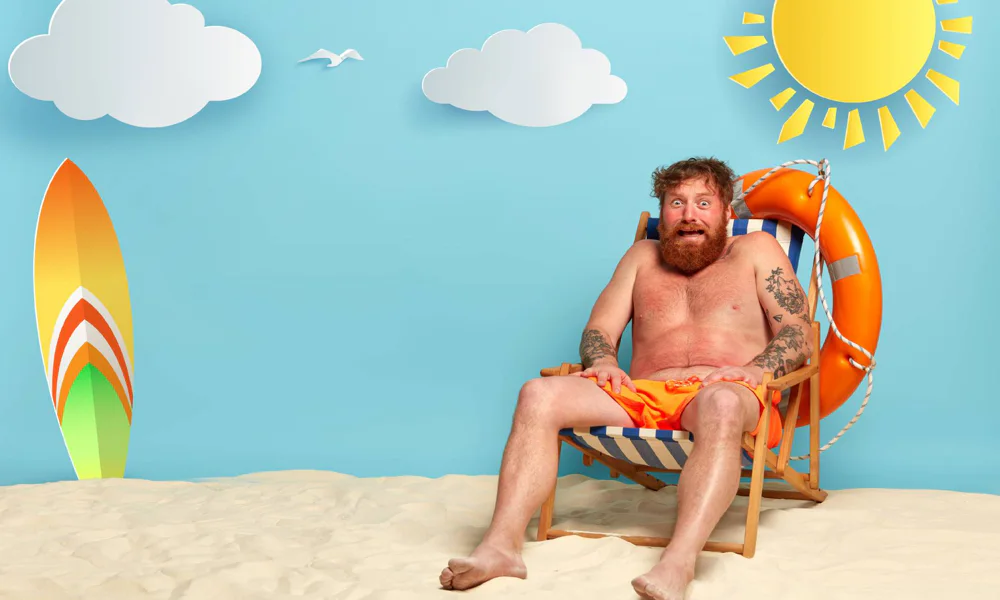 A bearded man with tattoos sitting on a beach chair under the sun, illustrating the need to avoid direct sunlight on fresh tattoos to prevent fading and sunburn.