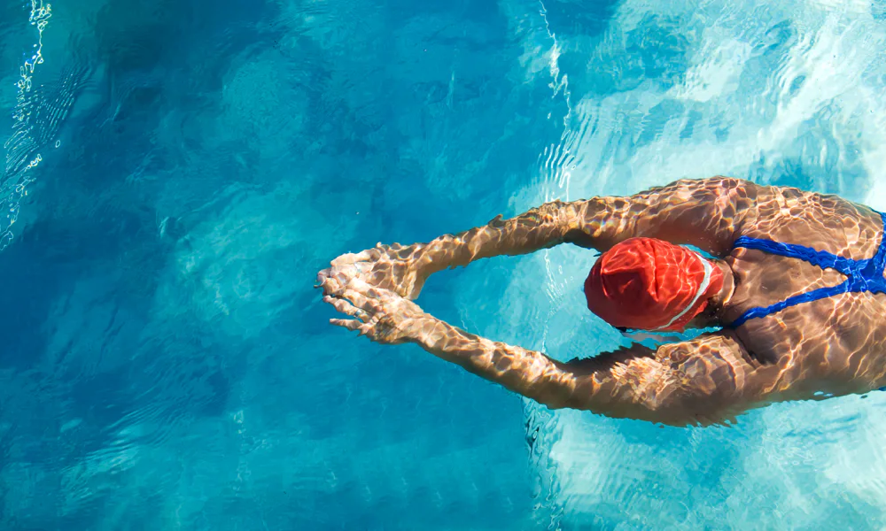 A swimmer diving into a pool, demonstrating the importance of avoiding swimming and soaking in water during the initial tattoo healing phase to prevent infection.
