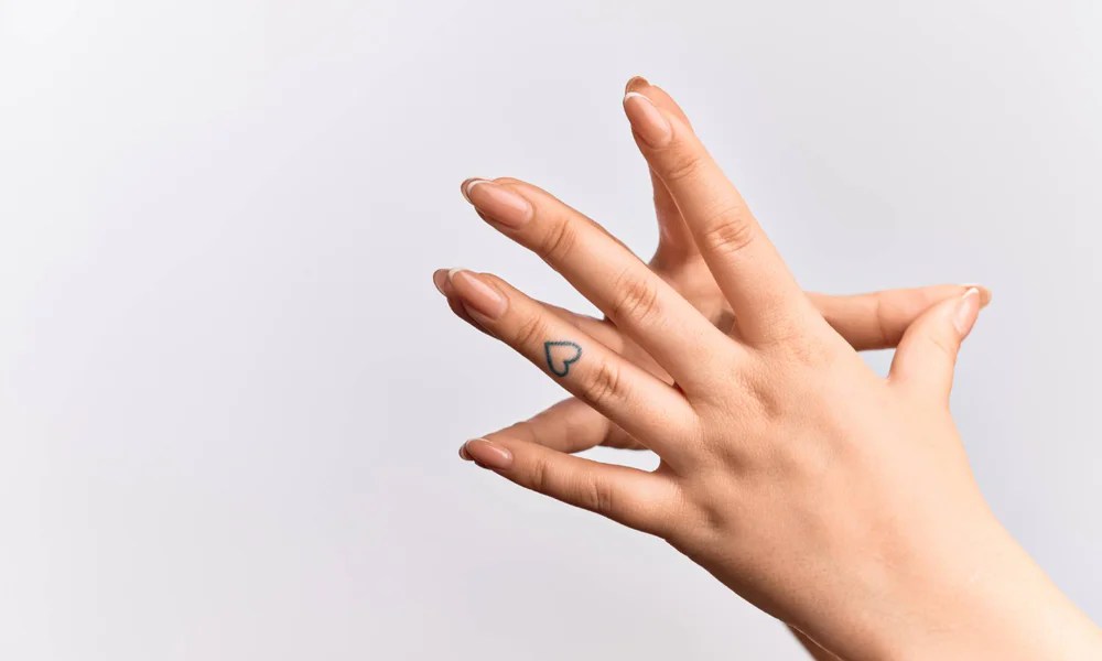 Hand with a minimalist heart tattoo on the side of the finger, with a light background