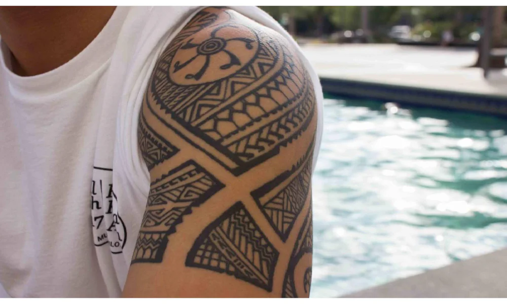 Close-up of a Polynesian tribal tattoo on a person's shoulder, featuring intricate black ink patterns symbolizing heritage and cultural significance.