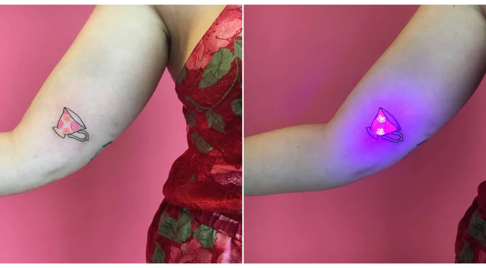 UV tattoo of a teacup on inner arm, glowing under blacklight, showing the effect of glow-in-the-dark ink on a delicate, colorful design.