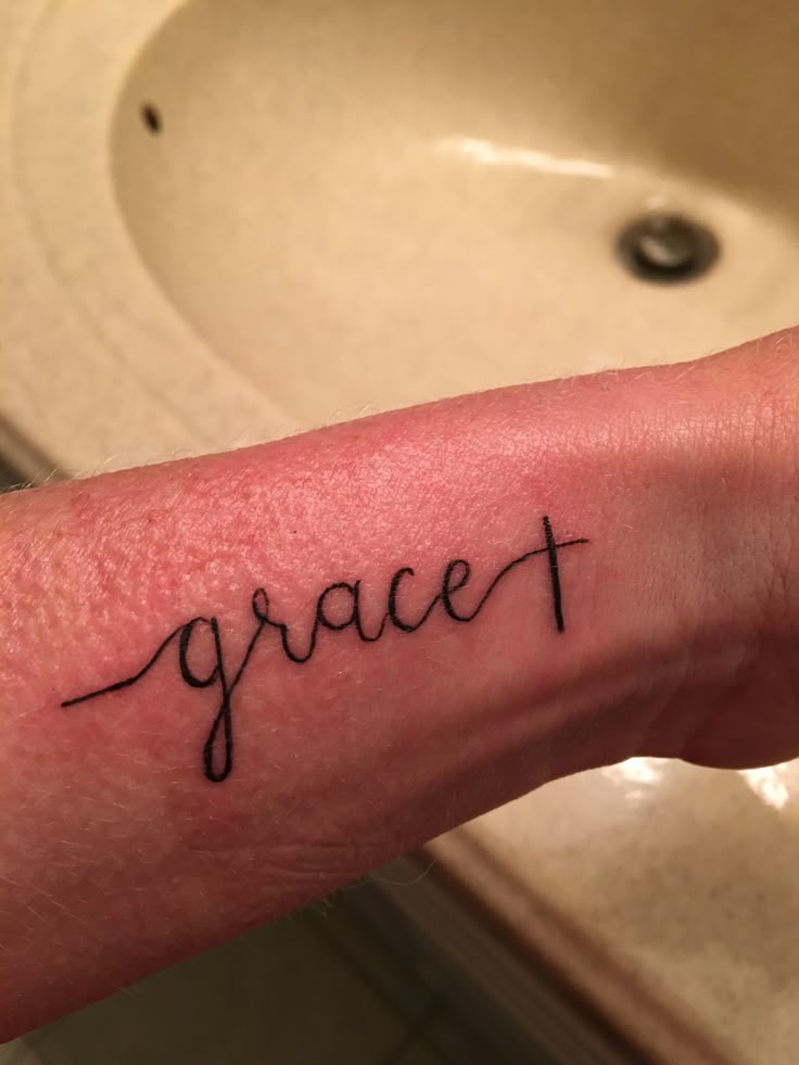 A simple grace tattoo with a cross at the end.