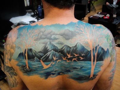 Mountain lake scene tattoo with cutout shapes on back